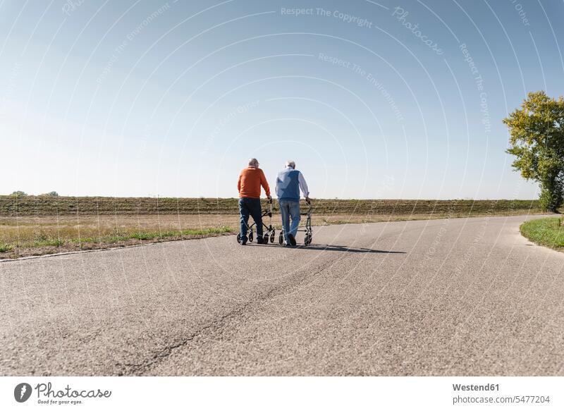 Two old friends walking on a country road, using wheeled walkers going bonding community Companionship sharing share togetherness age Stroll active seniors