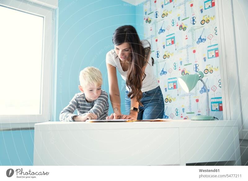 Mother helping son doing homework at desk sons manchild manchildren desks mother mommy mothers mummy mama Home work assistance assisting Help family families