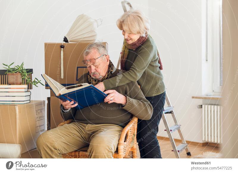 Senior couple looking at photo album surrounded by cardboard boxes in an empty room human human being human beings humans person persons caucasian appearance