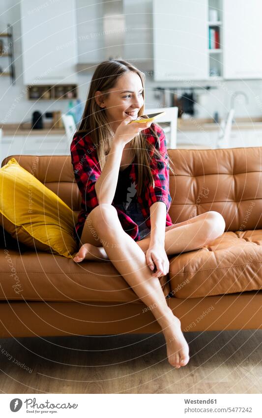 Happy young woman using cell phone on a couch at home human human being human beings humans person persons celibate celibates singles solitary people