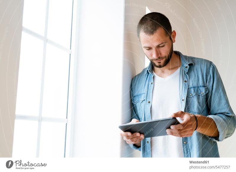 Young serious man at home looking at his tablet standing at window human human being human beings humans person persons short hairs short hairstyle
