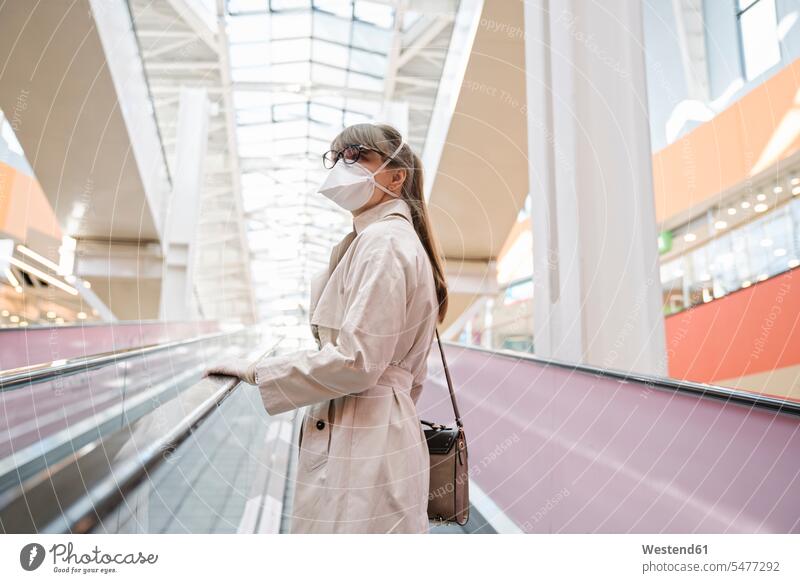 Woman with face mask and disposable gloves on an escalator in a shopping center bags hand-bag hand-bags handbags Eye Glasses Eyeglasses specs spectacles