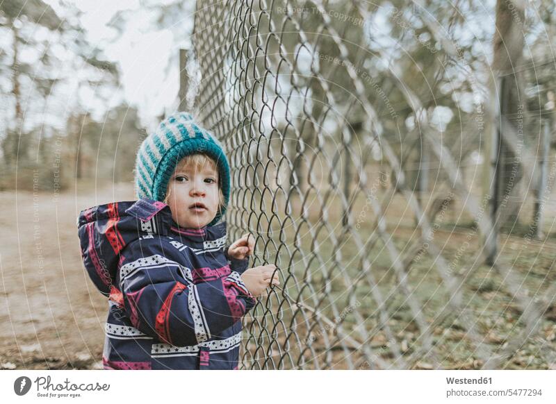 Portrait of toddler girl in warm clothes at a fence in forest woods forests females girls fences portrait portraits child children kid kids people persons