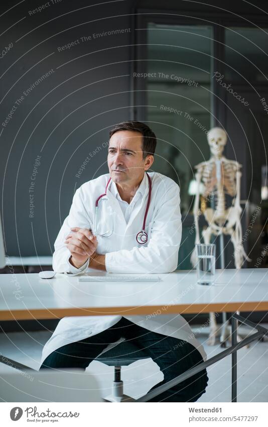 Doctor sitting at desk in medical practice with skeleton in background skeletons doctor physicians doctors medical practices Doctors Office Doctor's Office