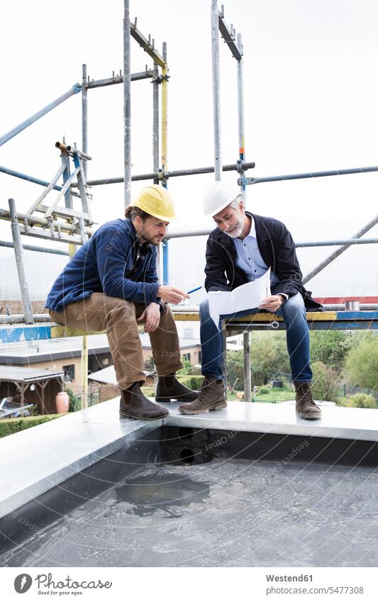 Architect and construction worker discussing blueprint while sitting on scaffold against clear sky color image colour image Germany Architecture