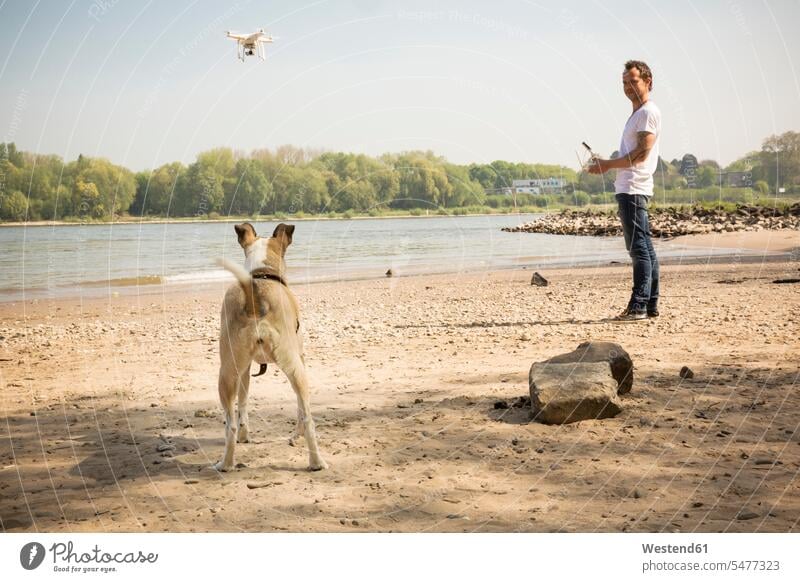 Man with a dog flying drone at a river River Rivers drones man men males dogs Canine water waters body of water Adults grown-ups grownups adult people persons
