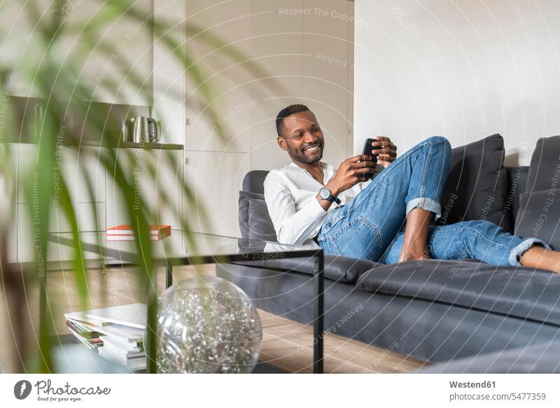 Portrait of smiling man sitting on couch in modern apartment using smartphone watches wrist watches Wristwatch Wristwatches couches settee settees sofa sofas