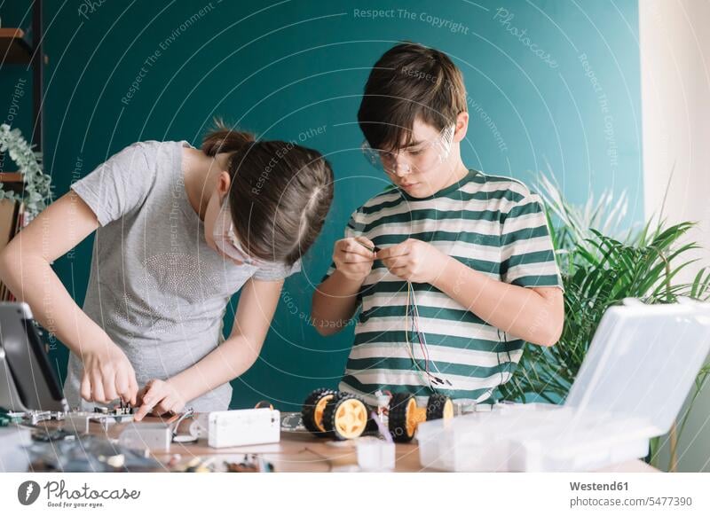 Siblings making robotic toy on table at home color image colour image indoors indoor shot indoor shots interior interior view Interiors casual clothing