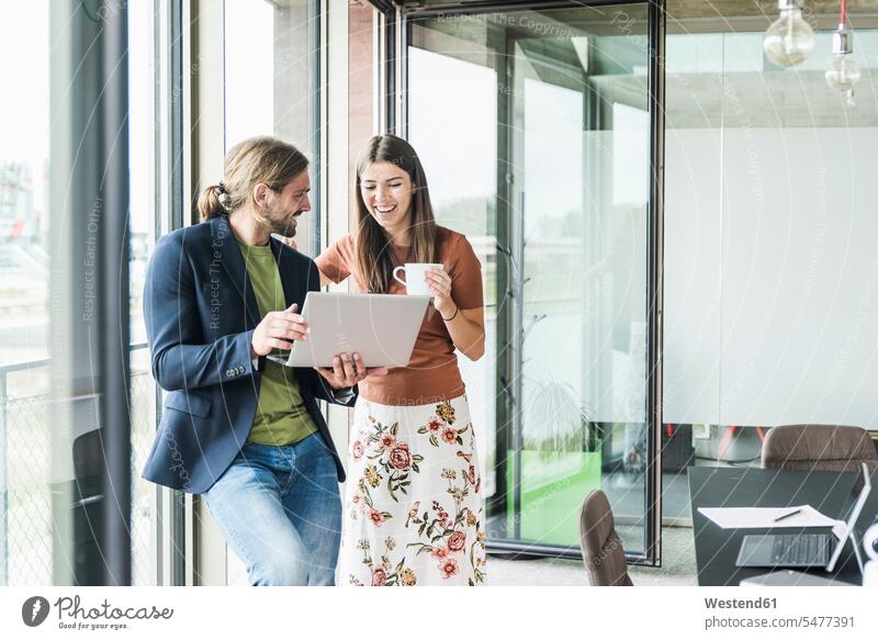 Happy young businesswoman and businessman using laptop at the window in office human human being human beings humans person persons caucasian appearance
