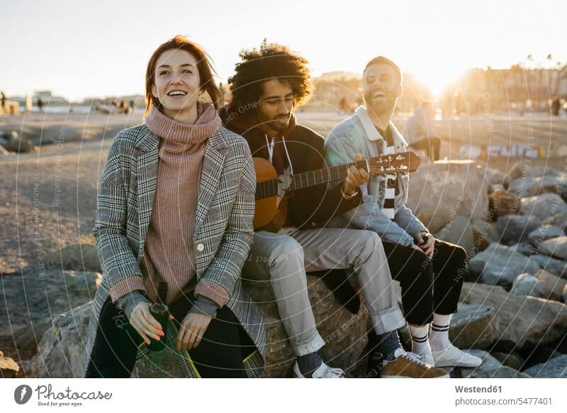 Three happy friends with guitar sitting outdoors at sunset Seated happiness sunsets sundown guitars atmosphere atmospheric mood moody Atmospheric Mood Vibe
