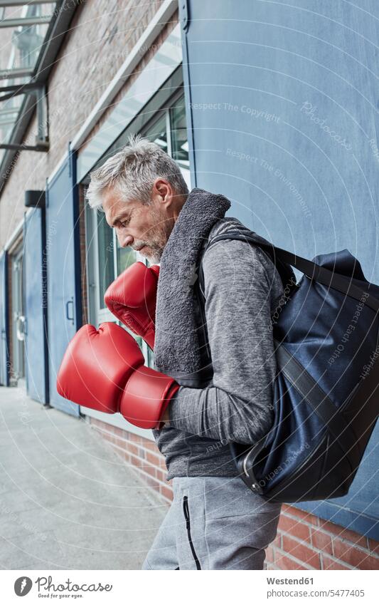 Mature man with towel, sports bag and red boxing gloves standing in front of gym towels Gym Bag men males gyms Health Club martial arts combative sport Adults