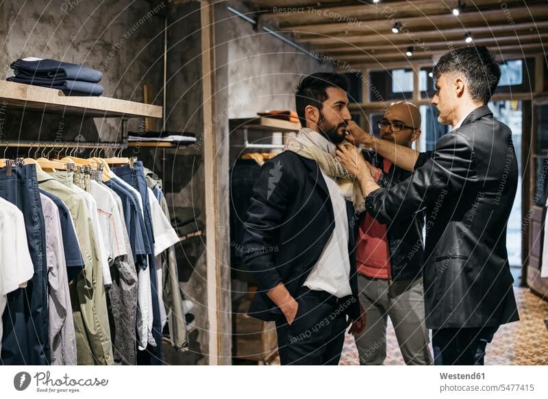 Two men working on new stylish look for handsome man in showroom customer clientele clients customers men's fashion shop modern contemporary males people