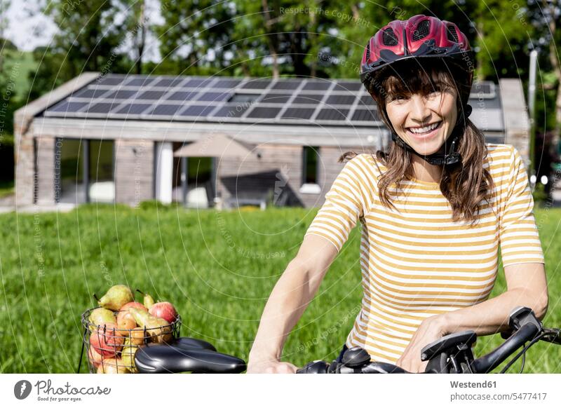 Portrait of happy woman with bicycle and organic fruit on a meadow in front of a house human human being human beings humans person persons caucasian appearance