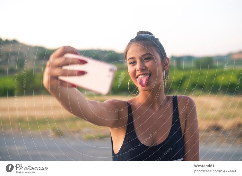 Portrait of teenage girl taking selfie with smartphone while sticking out tongue Selfie Selfies Teenage Girls female teenagers portrait portraits tongues