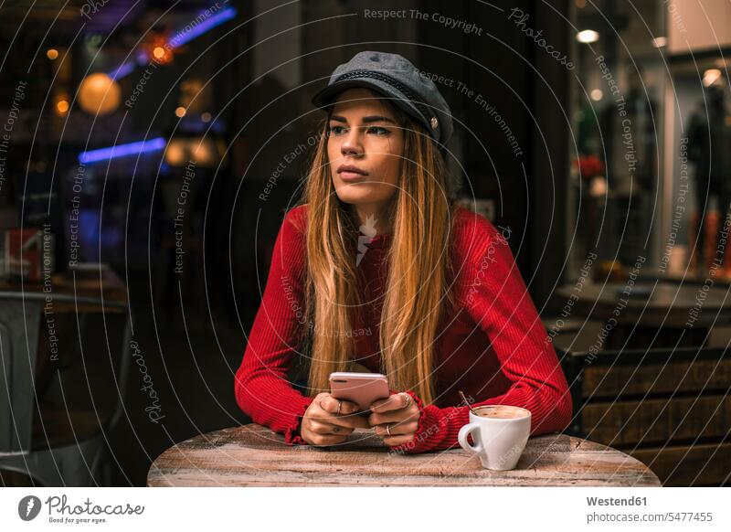 Portrait of pensive young woman with smartphone sitting on terrace of a coffee shop Cafe Shop Smartphone iPhone Smartphones Seated females women thoughtful