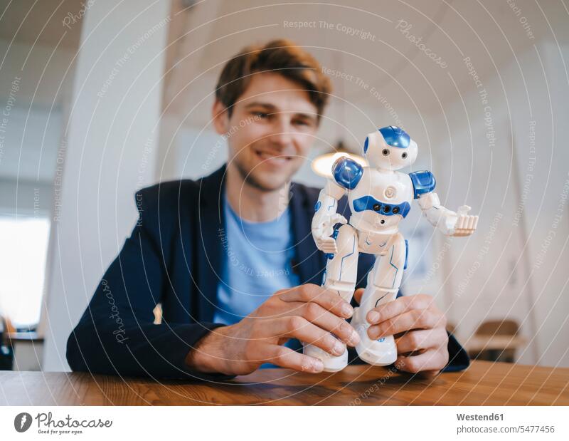 Smiling man holding robot men males Table Tables smiling smile robots Adults grown-ups grownups adult people persons human being humans human beings automaton