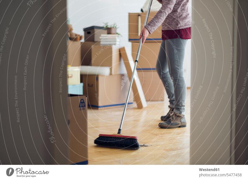 Woman sweeping the floor surrounded by cardboard boxes in an empty room human human being human beings humans person persons caucasian appearance