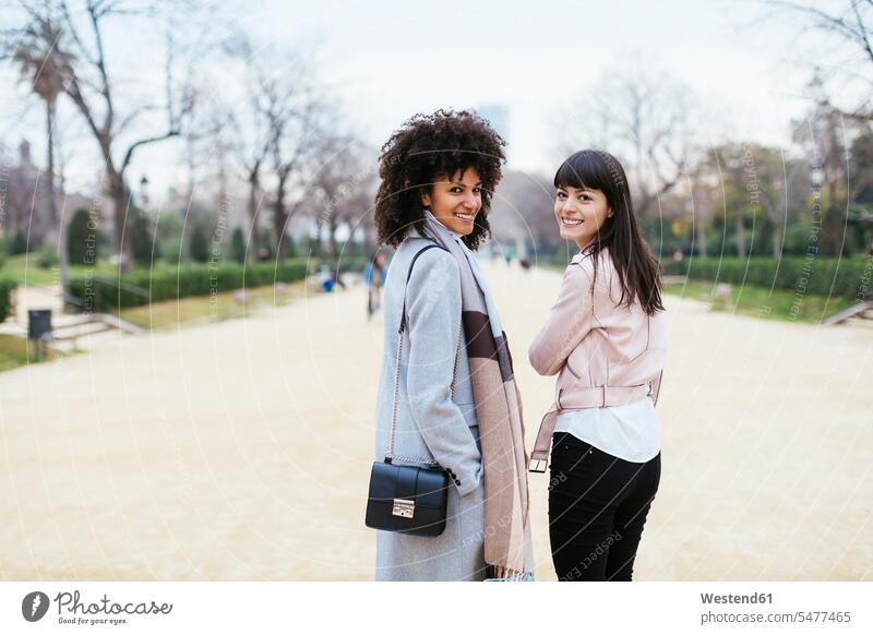 Spain, Barcelona, portrait of two smiling women in city park turning round female friends woman females town cities towns portraits parks turning around