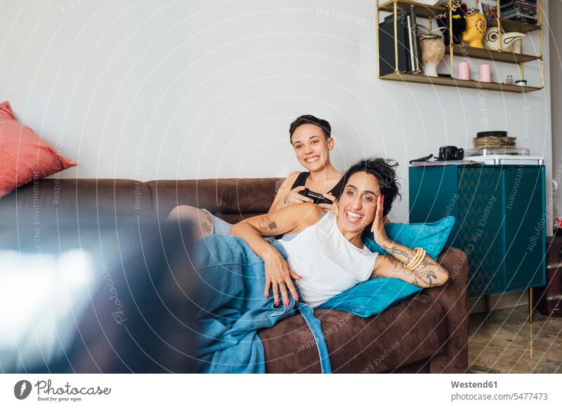 Smiling lesbian couple watching TV on sofa color image colour image indoors indoor shot indoor shots interior interior view Interiors day daylight shot