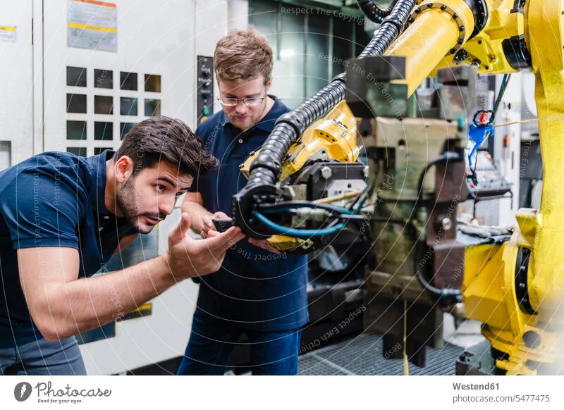 Male coworkers examining robotic arm while standing in manufacturing factory color image colour image indoors indoor shot indoor shots interior interior view