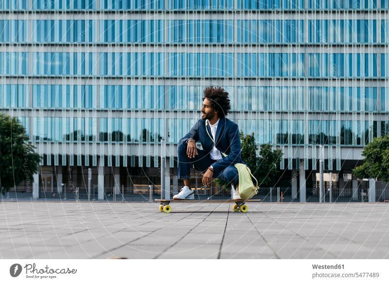 Spain, Barcelona, young businessman crouching on skateboard in the city Businessman Business man Businessmen Business men cowering males Skate Board skateboards