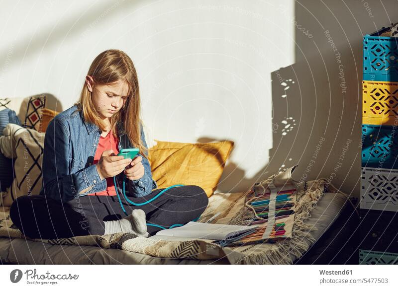 Girl sitting on bed at home doing homework and using smartphone Bed - Furniture beds pencil pencils pens telecommunication phones telephone telephones