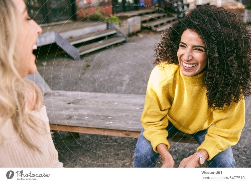 Cheerful female friends talking while sitting outdoors color image colour image Germany leisure activity leisure activities free time leisure time