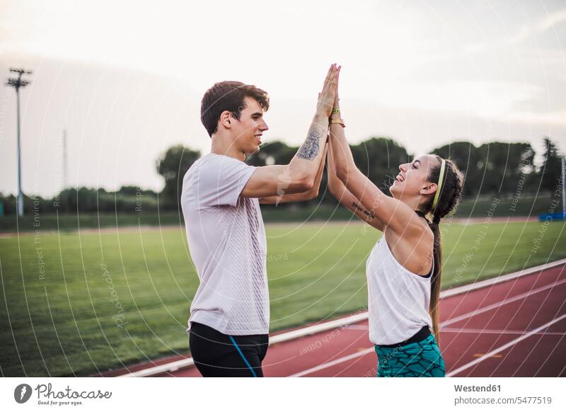 Male and female athlete high fiving on a tartan track smiling smile High Five Hi-Five high-fiving High-Five couple twosomes partnership couples athletes