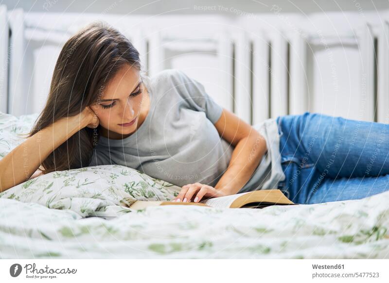 Young woman at home lying in bed reading book books females women beds laying down lie lying down Adults grown-ups grownups adult people persons human being