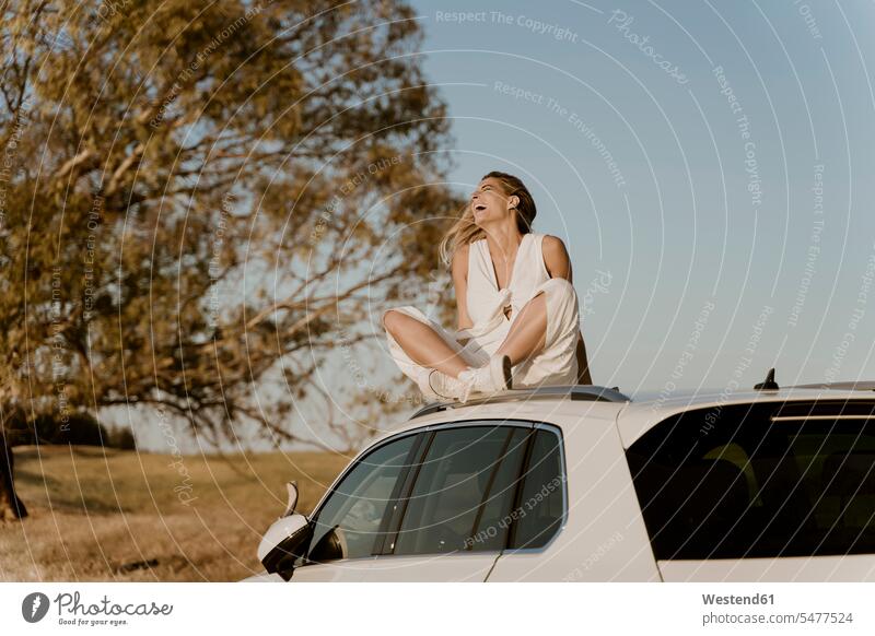 Laughing female traveller sitting on white car roof motor vehicles road vehicle road vehicles Auto automobile Automobiles cars motorcar motorcars smile Seated