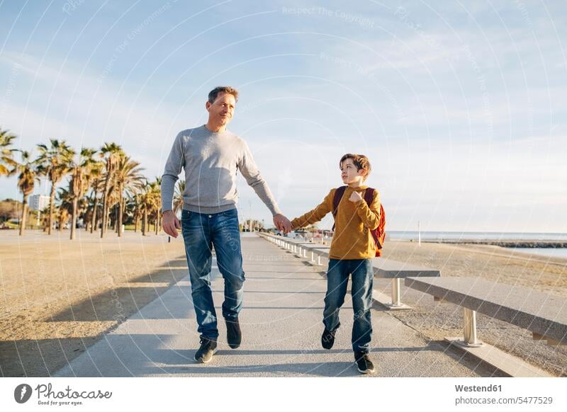 Father and son walking on beach promenade beaches going sons manchild manchildren father pa fathers daddy dads papa promenades family families people persons