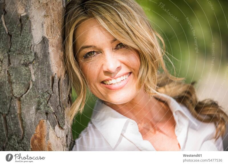 Happy mature businesswoman leaning on tree trunk during sunny day color image colour image outdoors location shots outdoor shot outdoor shots daylight shot
