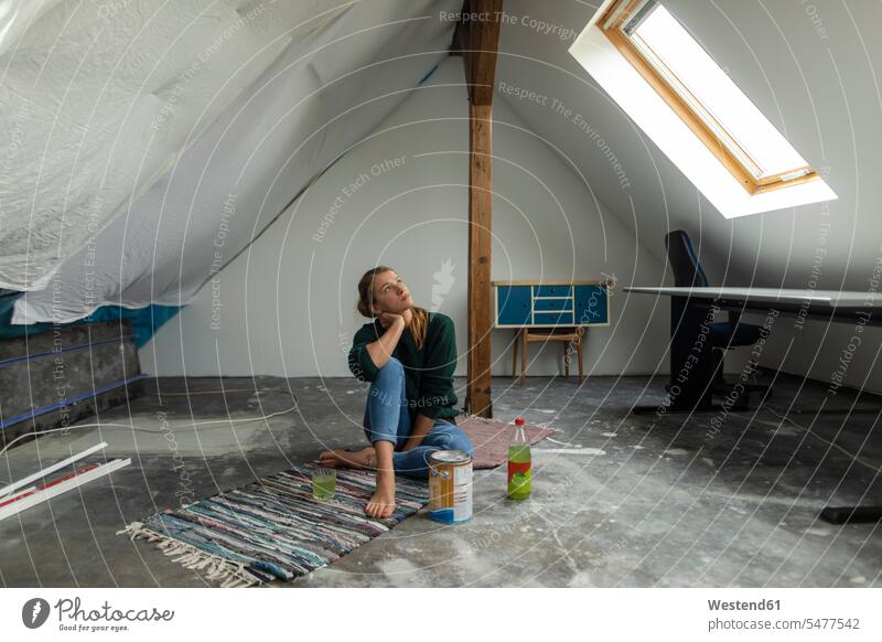 Young woman sitting on the floor in attic with paint bucket Germany apartment flats apartments soft drink refreshing drink soft drinks refreshing drinks