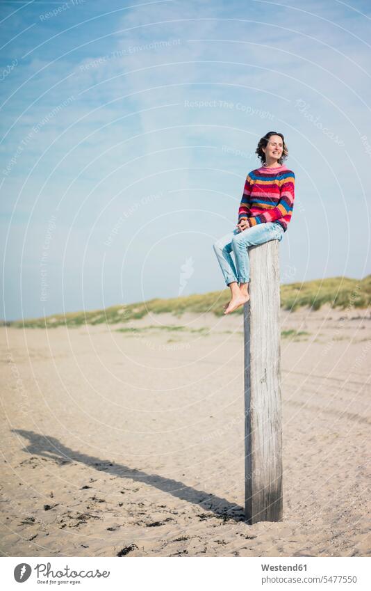 Mature woman sitting on a wood pole on the beach Seated independence independent beaches wood post Wooden Poles Netherlands The Netherlands Nederland Holland
