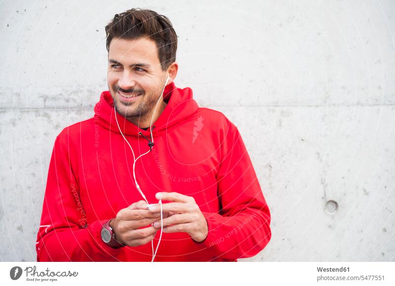 Portrait of sporty young man listening to music at a concrete wall relax relaxing hear smile delight enjoyment Pleasant pleasure colour colours sports athletes