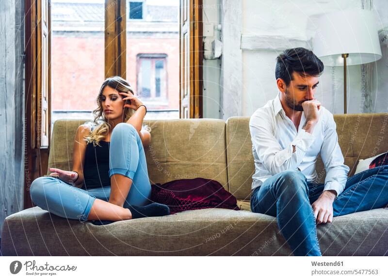 Couple sitting on sofa apart and being angry after quarrel couches settee settees sofas Seated bored boring anger annoyed morose Clash clashing Tension