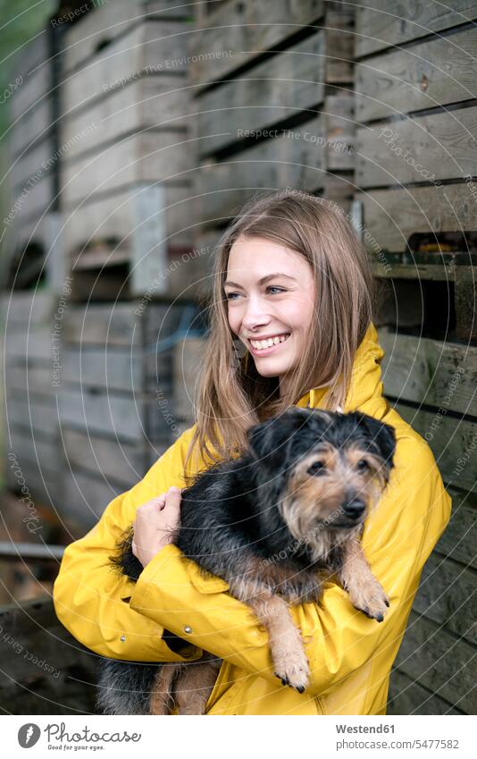 Smiling woman on a farm standing at wooden boxes holding dog dogs Canine smiling smile females women pets animal creatures animals agriculture Adults grown-ups
