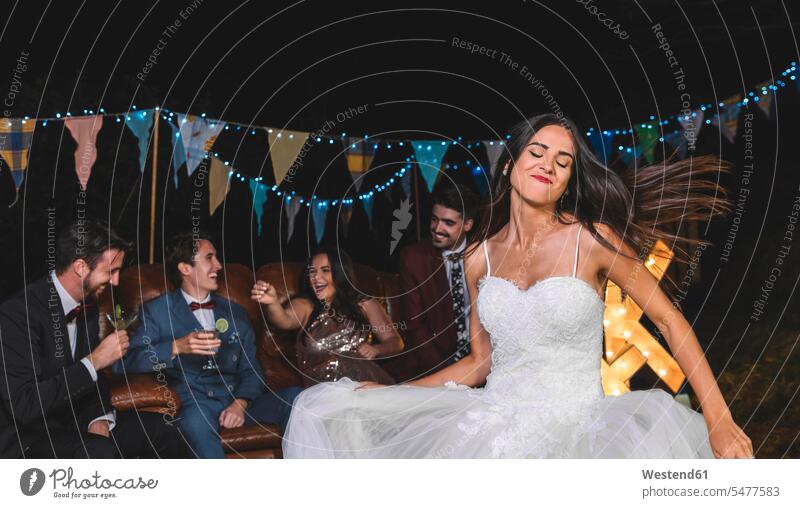 Happy bride dancing on a night field party with groom and friends in the background dance brides Wedding getting married marrying Marriage Party Parties