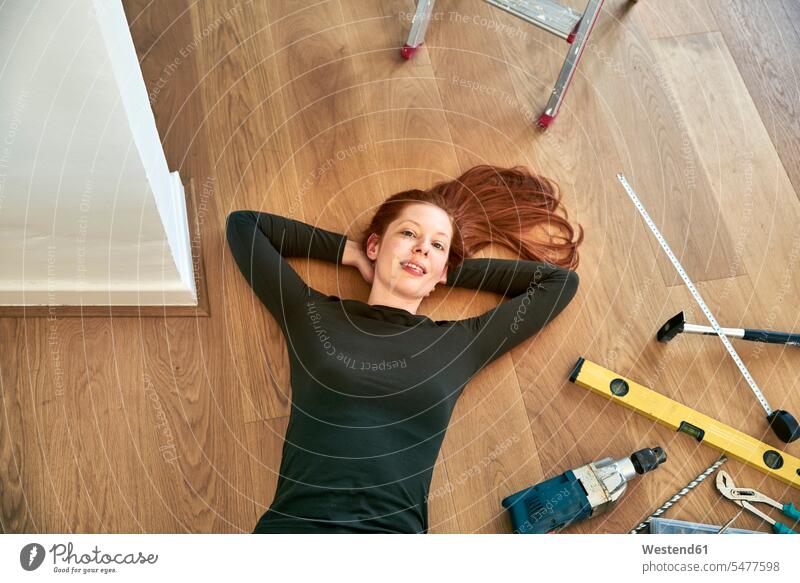 Redheaded woman lying beside tools on the floor Tool Kit laying down lie lying down Floor Floors redheaded red hair red hairs red-haired device devices floors
