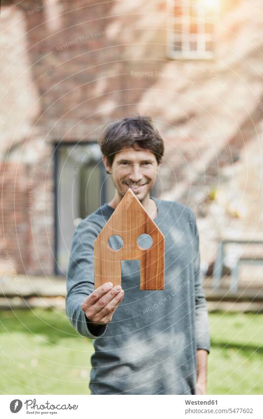Portrait of smiling man in front of his home holding house model houses models smile men males portrait portraits building buildings built structure