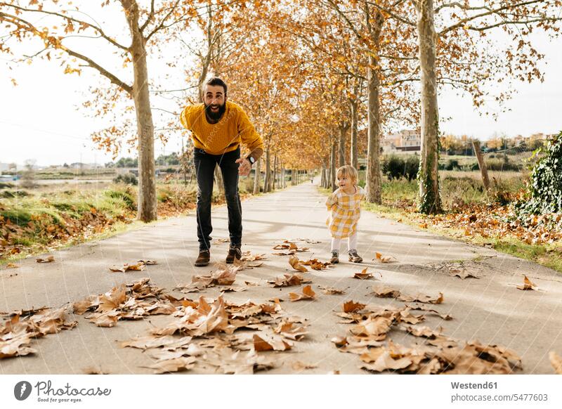 Father and daughter playing on a way in the park in autumn Leaf Leaves starting father fathers daddy dads papa daughters Joy enjoyment pleasure Pleasant delight