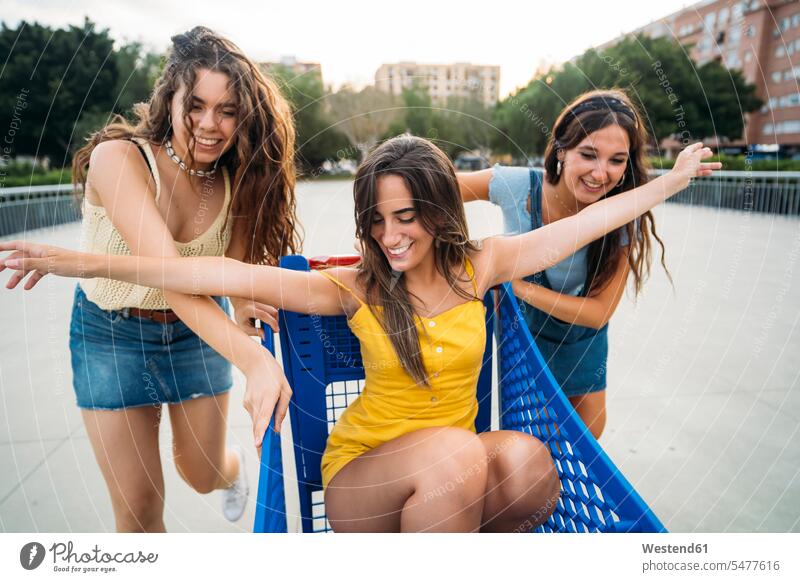 Three playful female friends with shopping cart in the city mate dark-haired brown haired brunette shopping trolley smile seasons summer time summertime summery