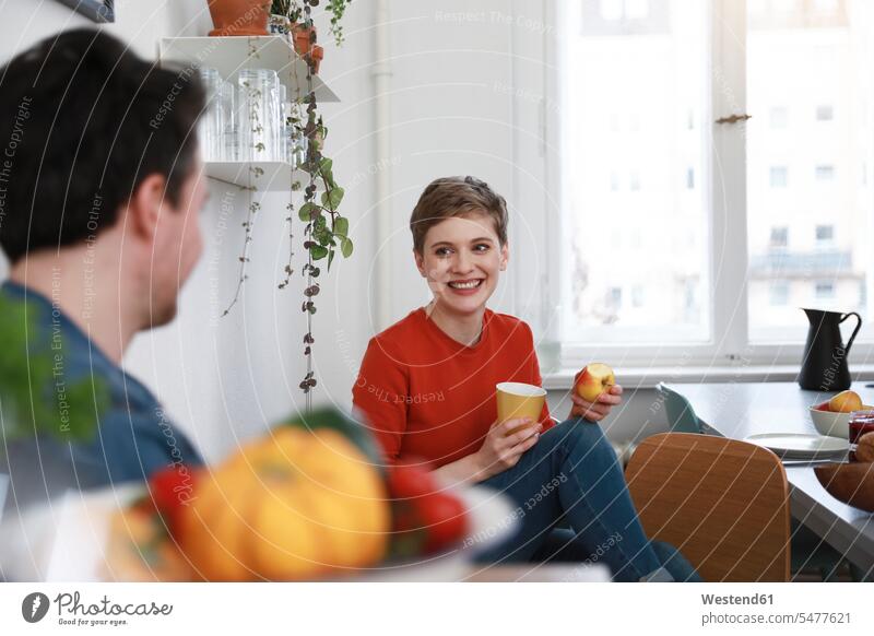couple sitting in kitchen, talking, woman eating apple domestic kitchen kitchens together speaking Seated happiness happy twosomes partnership couples home