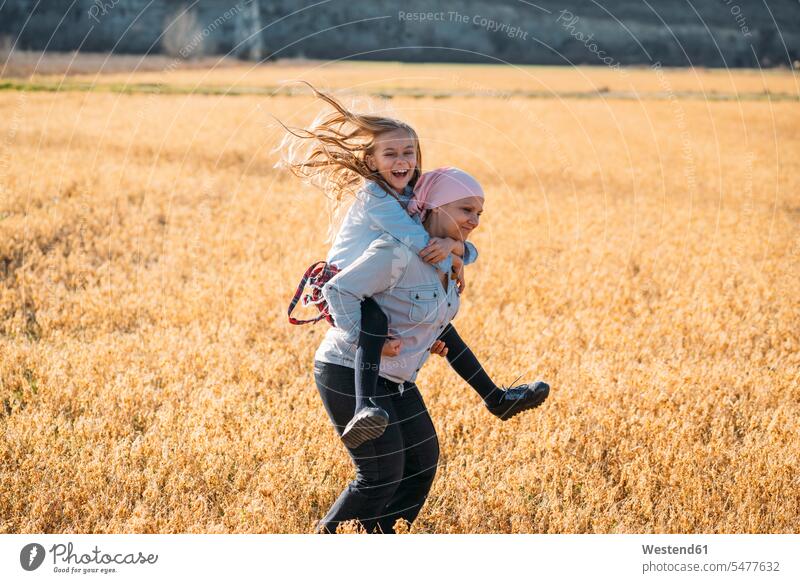 A woman with cancer carrying her daughter on her back, laughing human human being human beings humans person persons caucasian appearance caucasian ethnicity