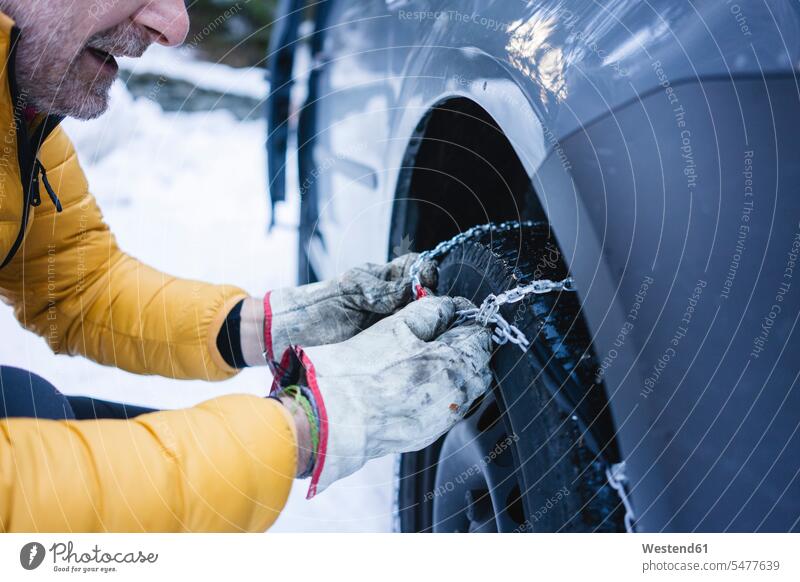 Man putting the snow chains on his car gloves coat coats jackets Auto automobile Automobiles cars motorcar motorcars Tire - Vehicle Part tires tyre tyres