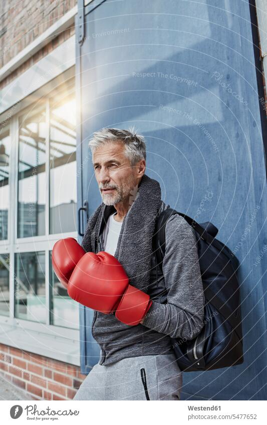 Portrait of mature man with towel, sports bag and red boxing gloves standing in front of gym towels Gym Bag portrait portraits men males gyms Health Club
