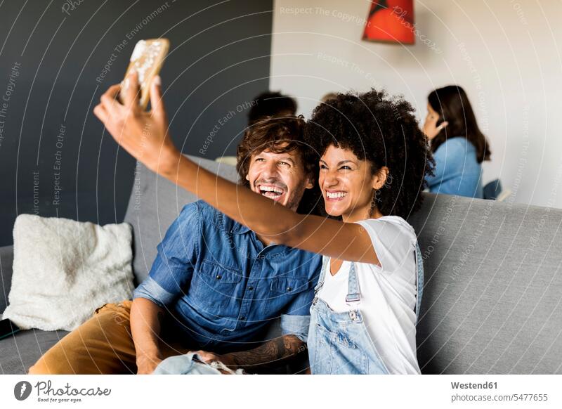 Happy couple sitting on couch taking a selfie happiness happy settee sofa sofas couches settees Selfie Selfies twosomes partnership couples Seated people
