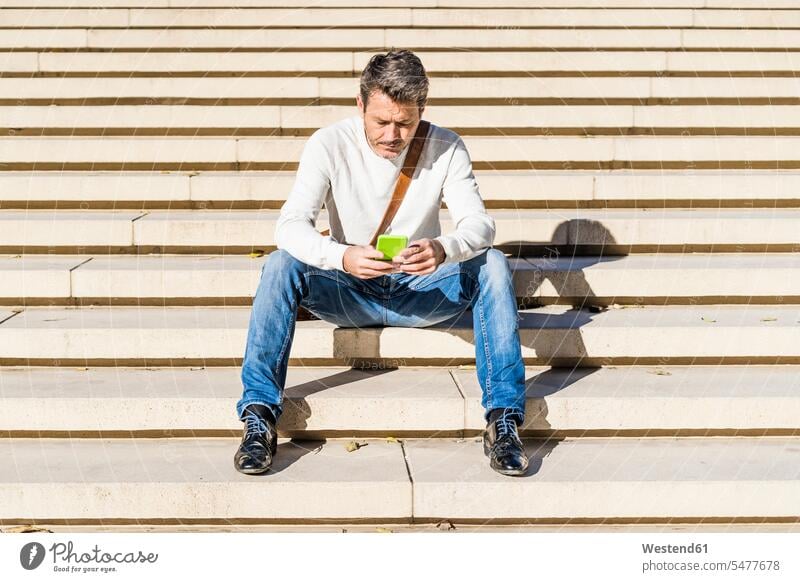 Casual businessman sitting on stairs, reading messages on his smartphone Businessman Business man Businessmen Business men mature men mature man stairway