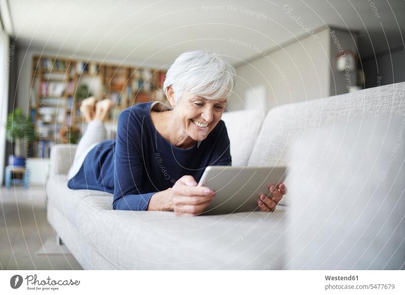 Senior woman using digital tablet lying on sofa at home color image colour image indoors indoor shot indoor shots interior interior view Interiors day