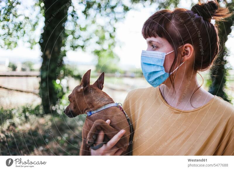 Young woman wearing face mask carrying dog while walking at park during COVID-19 color image colour image outdoors location shots outdoor shot outdoor shots day